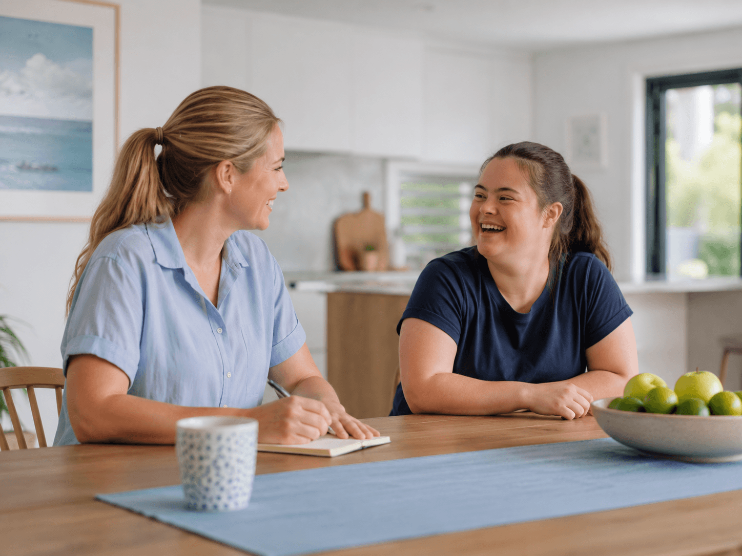 An Everbloom support worker and participant laughing together at a kitchen table